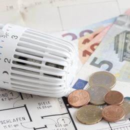 Heizungsthermostat mit Geldscheinen und Münzen auf einem Wohnungsgrundriss