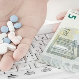 Tabletten und Geldschein in Hand vor Tastatur