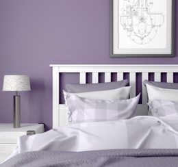 Schlafzimmer in den Farben lila/weiß mit Doppelbett, Nachtkästchen und Bild über dem Bett