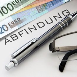 Schriftzug "Abfindung" zwischen Geldscheinen, Kugelschreiber und Sonnenbrille