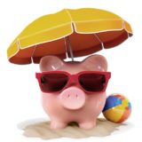 Sparschwein im Strandlook mit Sonnenbrille, Sonnenschirm und Wasserball auf Sand