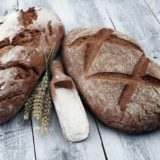 zwei Laib Brot liegen auf einem Holztisch mit einer Schaufel Mehl und Weizen