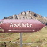 Wegweiser mit Schriftzug Apotheke steht in der Natur vor einem Berg