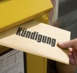 Hand steckt einen Brief mit der Aufschrift Kündigung in einen gelben Postkasten