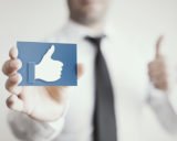 Mann hält Karte in der Hand, auf dem der Facebook-Like-Daumen abgebildet ist und hält seine andere Hand mit dem Daumen nach oben