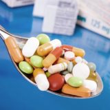 Tabletten auf einem Löffel mit Medikamentenverpackungen im Hintergrund
