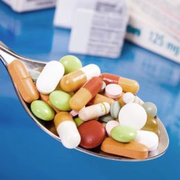Tabletten auf einem Löffel mit Medikamentenverpackungen im Hintergrund