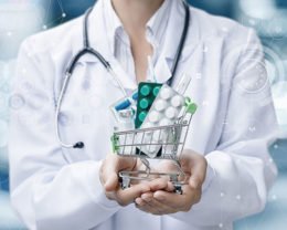Ein Arzt hält einen Miniatur-Einkaufswagen in der Hand, in dem sich Medikamente befinden