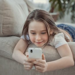 Kind liegt auf Sofa mit Smartphone