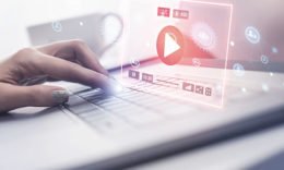 Eine Frauenhand tippt auf eine Tastatur über der ein Hologram eines Livesstreams schwebt