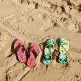 Zwei Paar Flip Flops, eines in rot, das andere in grün-gelb, am Strand