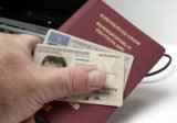 Eine Hand hält den neuen Personalausweis, dahinter den Führerschein sowie den Reisepass