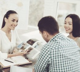 Frau im Reisebüro zeigt Paar einen Katalog