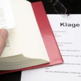 Klageschrift neben aufgeschlagenem Gesetz