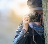 Frau fotografiert mit Kamera hinter Baum