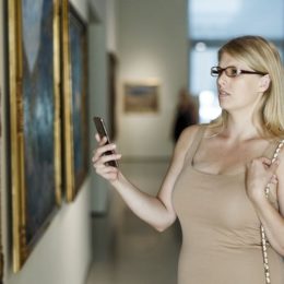 Frau fotografiert Bild in Museum mit Smartphone