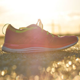 Pinker Laufschuh auf Asphalt mit dem Sonnenuntergang im Hintergrund