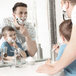 FotoliaVater und Sohn rasieren sich vor Spiegel