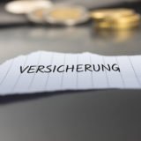 Fotolia_238641183: Versicherung auf einem Zettel mit Stift vor Geldmünzen