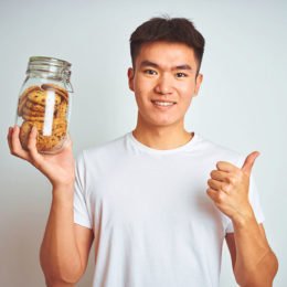 Fotolia_292787149: Junge hält ein Glasbehälter mit Cookies in der Hand und zeigt den Daumen nach oben