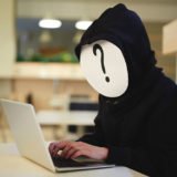 Person an einem Laptop mit einem Fragzeichen vor dem Gesicht