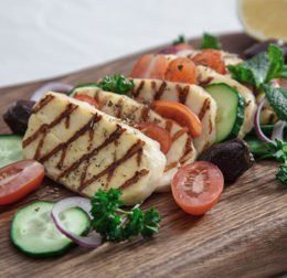 Gegrillter Halloumi-Käse auf einem Holzbrett mit Gurken und Tomaten ausgarniert