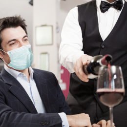Mann in Restaurant mit Maske Kellner schenkt Rotwein ein