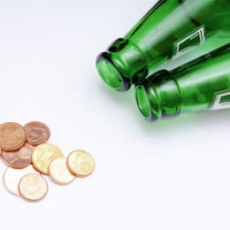 Geldmünzen liegen vor zwei grünen Pfandflaschen