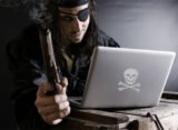 Pirat sitzt am Laptop mit qualmender Pistole in der Hand