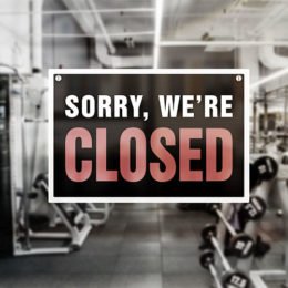 AdobeStock_368383781; Sorry, we are closed Schild vor verschwommenem Fitnessstudio.