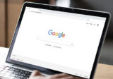 Google Suchmaschine auf Bildschirm von Laptop mit Hand auf Tastatur