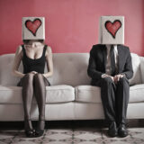 Mann und Frau sitzen auf einer Couch mit Herzen auf den Köpfen
