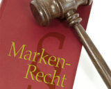 Ein hölzerner Richterhammer liegt auf einem roten Buch mit der Aufschrift Markenrecht