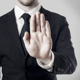 Mann in einem Anzug streckt seine Hand vor sich und symbolisiert die Aufforderung mit etwas aufzuhören.