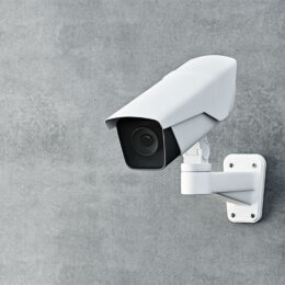 Eine weiße Überwachungskamera hängt an einer grauen Wand.