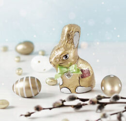 Goldener Schokoosterhase mit goldenen Schokoladeneiern vor einem blauen Hintergrund