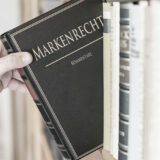 Eine Hand nimmt ein Buch mit der Aufschrift Markenrecht aus einem Regal