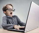 Ein Kind mit einer Brille sitzt schockiert vor einem Laptop