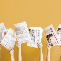 Hände halten Zeitungen vor einem gelben Hintergrund hoch