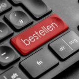 Es wird ein Ausschnitt einer schwarzen Tastatur gezeigt. Die rechte [Shift]-Taste ist durch eine rote Taste ersetzt, die den Schriftzug "bestellen" zeigt.