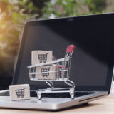 Mit Paketen gefüllter, kleiner Einkaufswagen steht auf Laptop