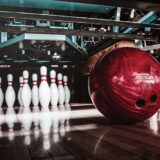 rote Bowlingkugel rollt auf Kegel zu