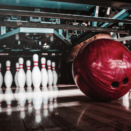 rote Bowlingkugel rollt auf Kegel zu