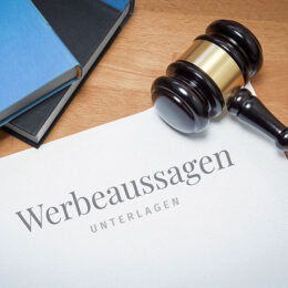 Werbeaussagen Unterlagen liegen neben Richterhammer auf einem Schreibtisch