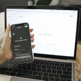 Laptop, vor den ein Smartphone gehalten wird. Auf beiden ist ChatGPT geöffnet.